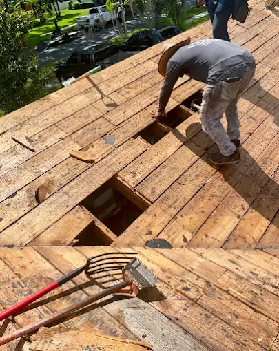 Worker exposing damaged roof decking during a repair